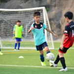 Boys playing soccer during a team training session outdoors on a sunny day.