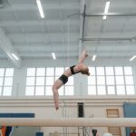 Young gymnast performs a backflip on a balance beam in an indoor gym.