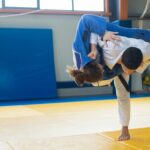 Two judokas practicing a powerful throw during judo training indoors on tatami mats.